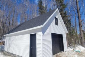 Dalle de béton monolithique. Revêtement extérieur en vinyle Gentek avec coin de vinyle. Soffite de 12’’ et fascia de 6’’ aluminium blanc. Toit habitable, pente 10/12 avec fenêtre de 24’’ x 30’’ en bardeaux d’asphalte IK0. Porte de garage en acier modèle Premium - noir 9’ x 7’, isolée R-16. Porte de service en acier – noir 34’’ x 82’’. Garage Le Supérieur, 18' x 23' x 9'