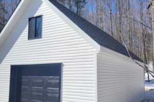 Dalle de béton monolithique. Revêtement extérieur en vinyle Gentek avec coin de vinyle. Soffite de 12’’ et fascia de 6’’ aluminium blanc. Toit habitable, pente 10/12 avec fenêtre de 24’’ x 30’’ en bardeaux d’asphalte IK0. Porte de garage en acier modèle Premium - noir 9’ x 7’, isolée R-16. Porte de service en acier – noir 34’’ x 82’’. Garage Le Supérieur, 18' x 23' x 9'