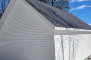 Dalle de béton monolithique. Revêtement extérieur en vinyle Gentek avec coin de vinyle. Soffite de 12’’ et fascia de 6’’ aluminium blanc. Toit habitable, pente 10/12 avec fenêtre de 24’’ x 30’’ en bardeaux d’asphalte IK0. Porte de garage en acier modèle Premium - noir 9’ x 7’, isolée R-16. Porte de service en acier – noir 34’’ x 82’’. Garage Le Supérieur, 18' x 23' x 9'