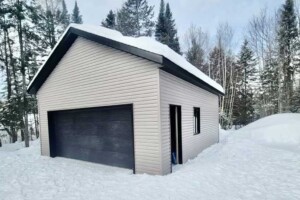 Dalle de béton de 6’’. Revêtement extérieur en vinyle Gentek avec coin de vinyle. Soffite de 12’’ et fascia 6’’en aluminium noir. Toit standard, pente 6/12 en bardeaux d’asphalte IKO. Porte de garage en acier double modèle GARAGA – noir 16’ x 7’, isolée R-16. Fenêtre aluminium à battant 36’’ x 40’’. Porte de service en acier – noir 34’’ x 82’’avec fenêtre guillotine. Garage Le Standard, 22' x 26' x 10'