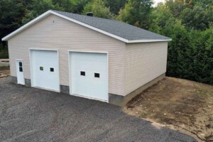 Dalle de béton 8’’ avec retour de fondation de 24’’. Revêtement extérieur en vinyle Gentek avec coin de vinyle. Soffite de 12’’ et fascia de 6’’en aluminium blanc. Toit standard, pente 5/12 en bardeaux d’asphalte IK0. 2 portes de garage en acier modèle Urbain-blanc 10’ x10’ avec fenêtres dans le panneau du centre incluant moteur électrique, isolée R-16. Fenêtre aluminium 60’’x48’’ à battant. Une porte de service standard en acier - blanc 34’’ x 82’’avec fenêtre à guillotine en façade du garage. Garage Commercial - Le Jumeau, 36' x 30' x 10'