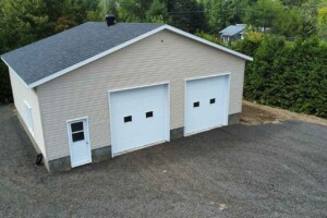 Dalle de béton 8’’ avec retour de fondation de 24’’. Revêtement extérieur en vinyle Gentek avec coin de vinyle. Soffite de 12’’ et fascia de 6’’en aluminium blanc. Toit standard, pente 5/12 en bardeaux d’asphalte IK0. 2 portes de garage en acier modèle Urbain-blanc 10’ x10’ avec fenêtres dans le panneau du centre incluant moteur électrique, isolée R-16. Fenêtre aluminium 60’’x48’’ à battant. Une porte de service standard en acier - blanc 34’’ x 82’’avec fenêtre à guillotine en façade du garage. Garage Commercial - Le Jumeau, 36' x 30' x 10'